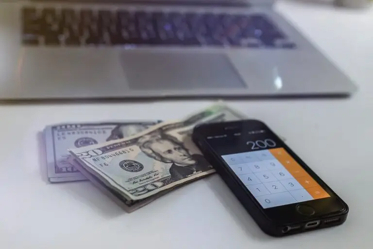 Imagem de uma calculadora, notas de dólar e um notebook que ilustra um cálculo de spread cambial em ums operação de câmbio, como o envio ou recebimento de uma remessa internacional o pagamento de uma invoice, o recebimento de uma exportações, entre outros tipos de transferências internacionais.