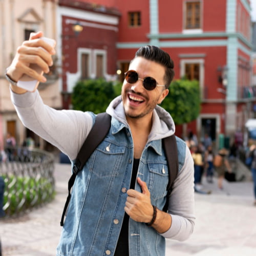 Imagem de um turista fazendo uma selfie sorrindo. Para fazer uma viagem internacional é necessário um serviço de câmbio.