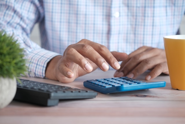 Imagem de um homem mexendo na calculadora. Nesse contexto, a imagem ilustra um profissional financeiro fazendo contas e simulações de câmbio para empresas.