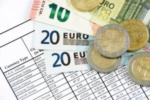Nesta imagem, temos uma planilha com valores em moeda estrangeira e notas de euros para simbolizar a aplicação do IOF no câmbio.