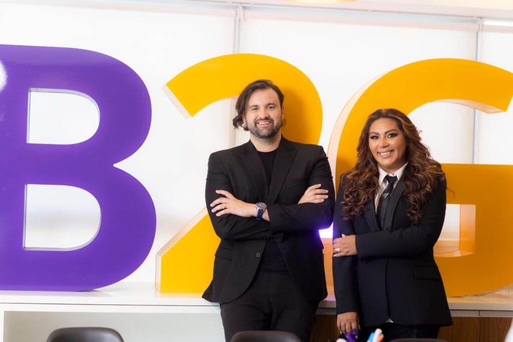 Na imagem, estão lado a lado, da esquerda para a direita, sorrindo, o Diego Zia e a Janaina Assis, sócios-fundadores da B2Gether, empresa referência em operações de câmbio no Brasil. A imagem informa uma notícia importante: a B2Gether foi selecionada pela Apex Brasil para integrar a plataforma Brasil Exportação.