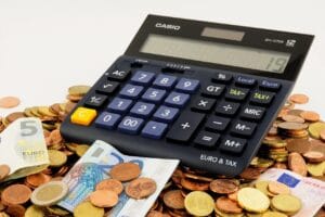 Imagem de uma calculadora em meio a notas e moedas moedas estrangeiras. Essa imagem ilustra o cálculo de taxas ocultas no câmbio.